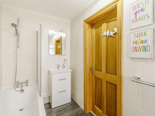 A bathroom with a shower, a sink, a mirror, and a wooden door.