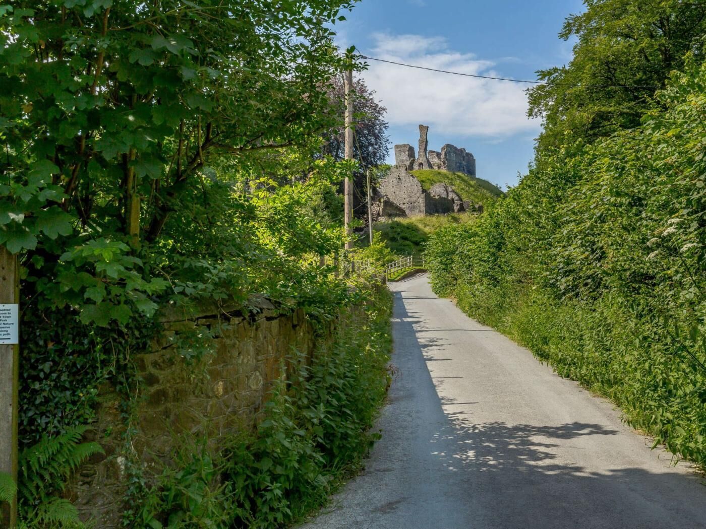 Eine schmale Straße, gesäumt von üppiger Vegetation und Steinmauern, die zu einem historischen Steinbau führt.