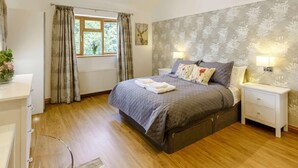 A bedroom with a bed, bedside tables, a window with curtains, a radiator, and a wall with a floral pattern. - 4 Bed in Okehampton (oc-83785) (Okehampton)