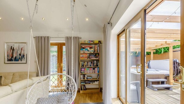 A modern living room with a hanging chair, a bookshelf, and a sliding glass door leading to an outdoor patio. - 4 Bed in Okehampton (oc-83785) (Okehampton)