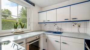 Eine Küche mit weißen Schränken, einer blauen Arbeitsplatte, einem Fenster mit Pflanzen und einem eingebauten Backofen.