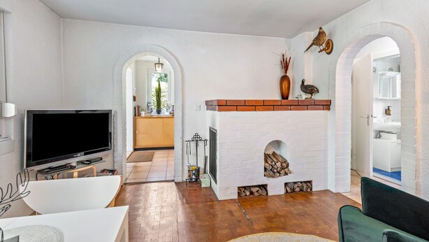 Ein Wohnzimmer mit Fernseher, Kamin und Bogen, der in andere Räume führt.