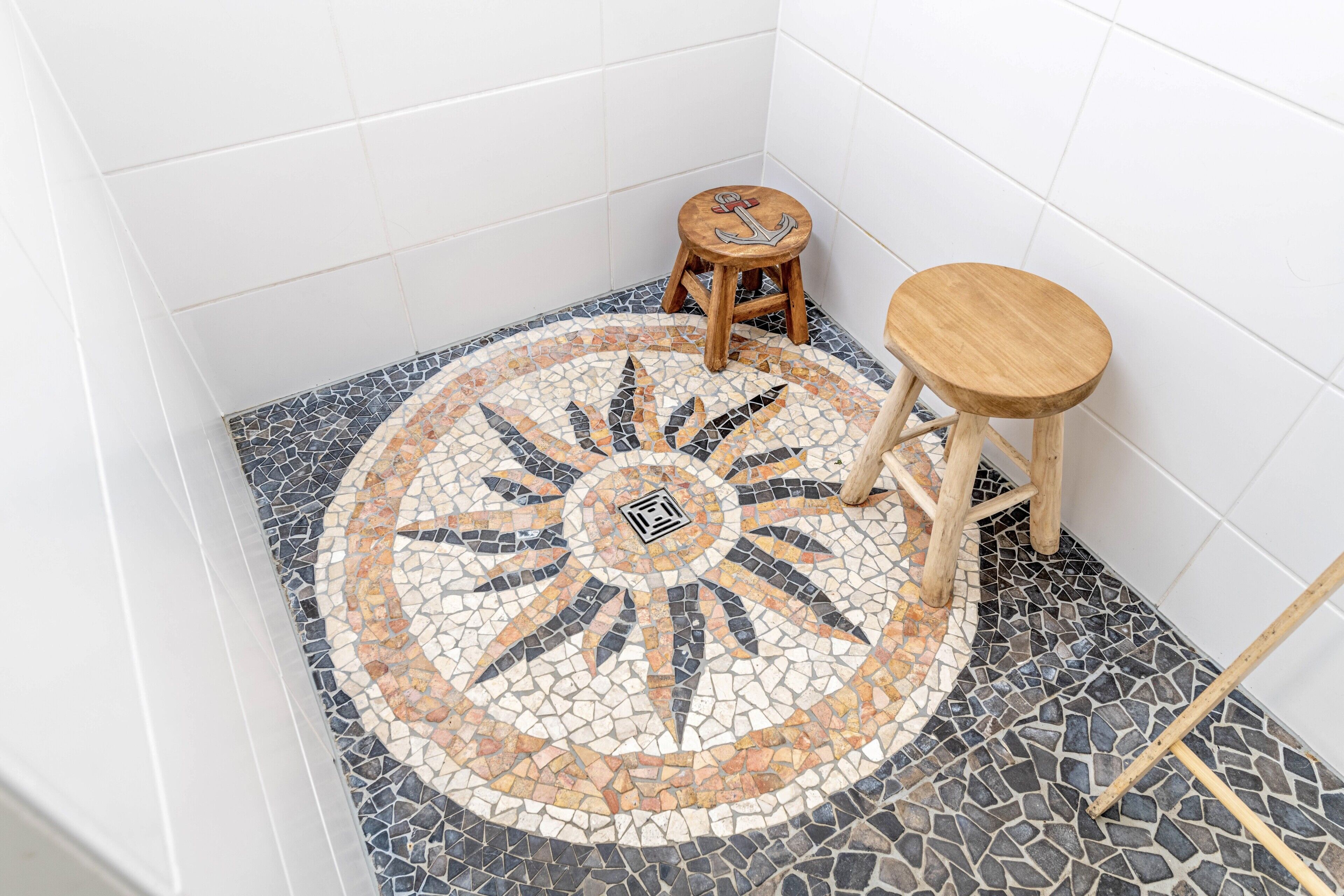 A bathroom with a mosaic floor, two wooden stools, and a wooden bench.