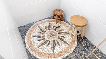 A bathroom with a mosaic floor, two wooden stools, and a wooden bench.