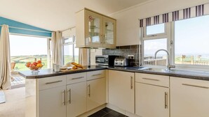 A modern kitchen with a view of the countryside, a microwave, toaster, and a fruit bowl. - 3 Bed in Torpoint (oc-83792) (Millbrook)