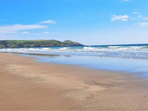 Ein Strand mit Wellen, einem klaren Himmel und sanften Hügeln im Hintergrund.