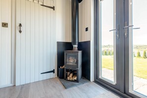 Ein Zimmer mit Kaminofen, weißen Wandverkleidungen, einer Schiebetür zum Garten und einem Holzboden.