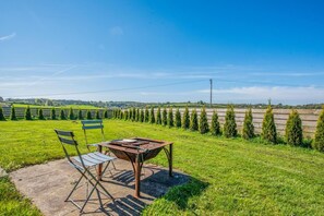 A patio with a table and chairs, a wooden bench, and a view of a green field with rows of trees. - 1 Bed in Narberth (oc-83862) (Whitland)