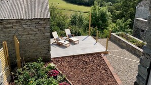 Un bâtiment en pierre doté d’une terrasse, de deux chaises longues et offrant une vue sur un paysage verdoyant.