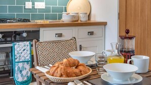 Une cuisine équipée d’une cuisinière, de placards, d’un plan de travail carrelé et de divers éléments pour le petit-déjeuner, comme des croissants, des bols et une machine à café.
