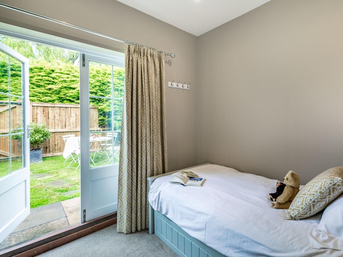 A bedroom with a bed, a window with curtains, and a view of a garden.