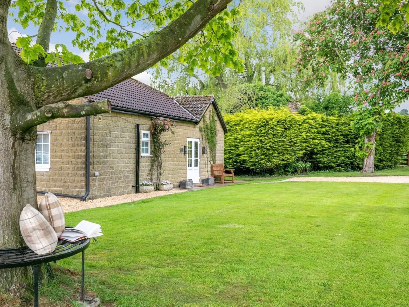 A stone house with a tiled roof, a lawn, and a bench with cushions.
