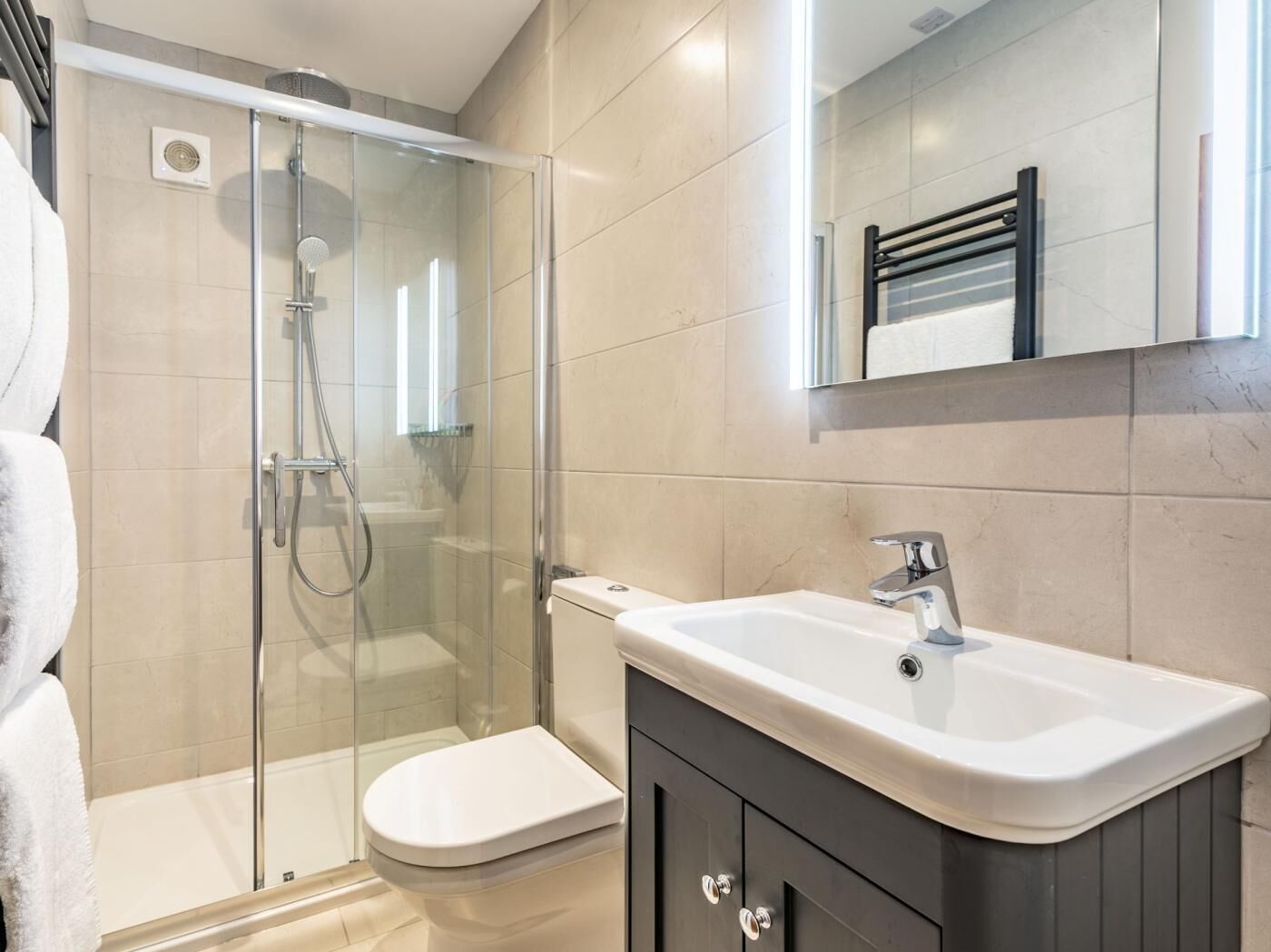 Un baño moderno con cabina de ducha de vidrio, inodoro blanco, tocador con lavabo y espejo.