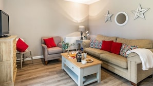 Ein Wohnzimmer mit Sofa, Sessel, Couchtisch und Fernseher.