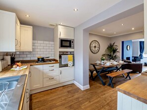A modern kitchen with white cabinets, a microwave, and a stove. There's a dining area with a table set for two, a clock, and a potted plant. - 3 Bed in Filey (oc-84007) (Filey)
