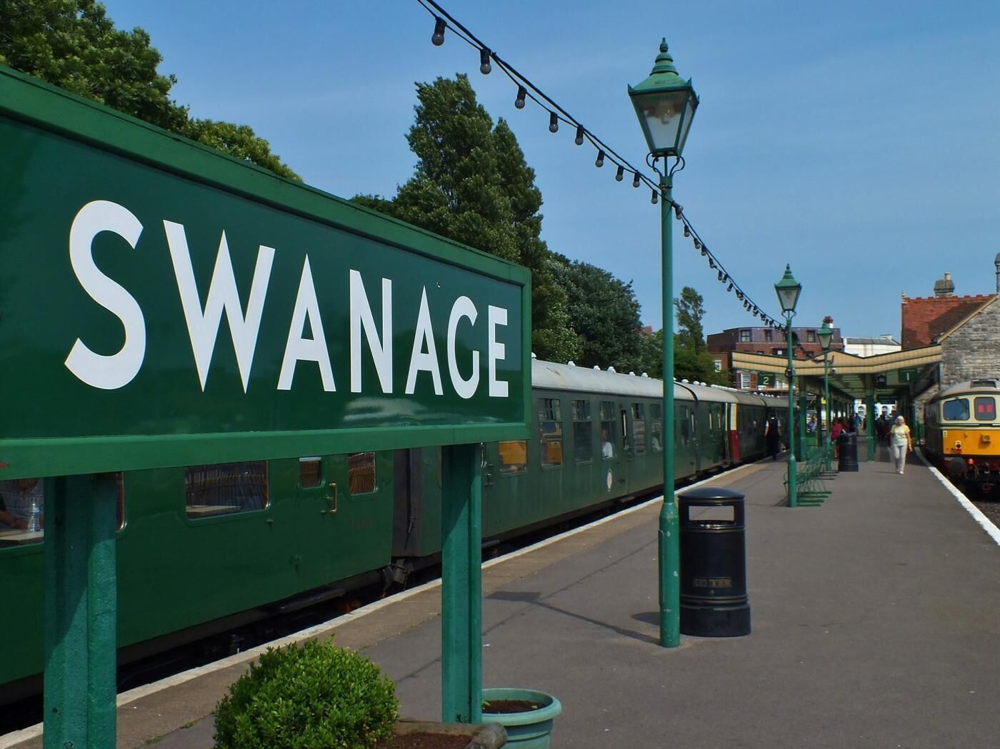 Uma plataforma de estação de trem com uma placa verde indicando 'SWANACE'.