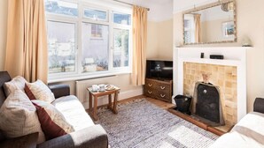 Een woonkamer met een bank, een televisie, een open haard en een raam met gordijnen.
