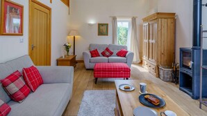 Una sala de estar acogedora con un sofá, un reposapiés de cuadros rojos, un armario de madera y una chimenea.