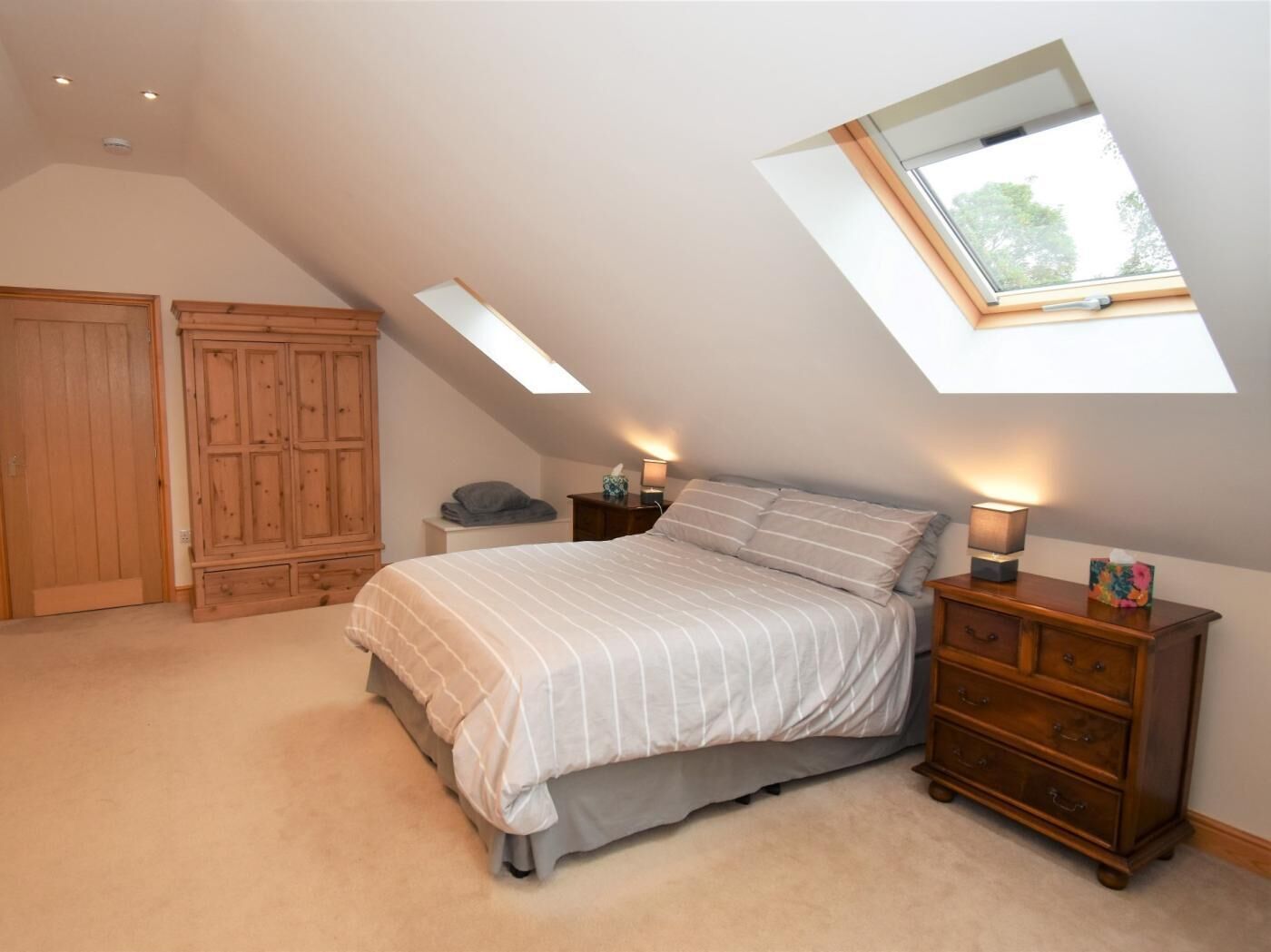 A bedroom with a sloped ceiling, a bed, a nightstand, a dresser, and a wardrobe.