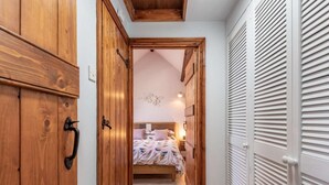 Un corridoio stretto che conduce a una camera da letto con un letto, un'armadiatura in legno e un guardaroba bianco con persiane orizzontali.