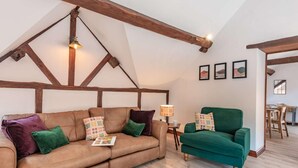 Una stanza in stile loft con travi a vista in legno, un divano in pelle marrone, una poltrona verde e un tavolino con una lampada.