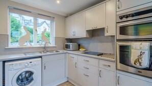 Eine kompakte Küche mit Waschmaschine, Mikrowelle, Backofen und einem Fenster mit Blick auf Häuser.