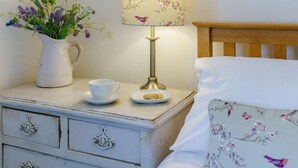 Ein Schlafzimmer mit einem hölzernen Kopfteil, einem Nachttisch mit Lampe, einer Vase mit Blumen, einer Tasse und einem Teller mit einem Keks.