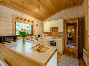 A wooden cabin interior with a kitchen area, a dining table with a sandwich, and a window with flowers.