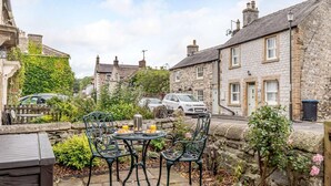 A stone building with a stone wall, a metal table with chairs, and a car parked in the background. - 2 Bed in Bakewell (oc-85314) (Ashford in the Water)