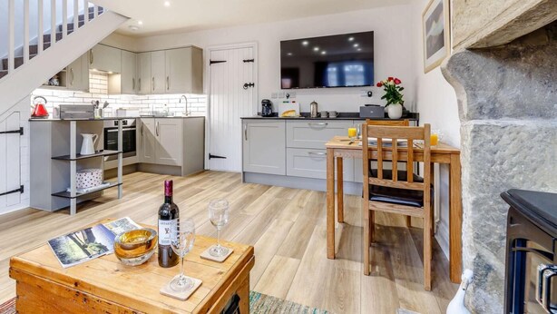 A modern kitchen with a dining area, a TV mounted above the counter, and a stone fireplace. - 2 Bed in Bakewell (oc-85314) (Ashford in the Water)