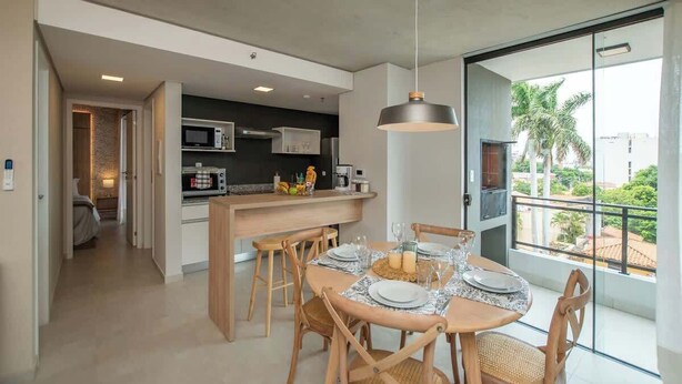A modern kitchen with a central island, dining area with a round table, and a balcony with a view. - Corporate Stays Insignia City - A43 (Asunción)