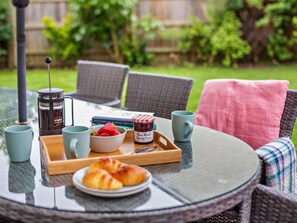 Ein runder Glastisch mit einer Tablett, auf dem eine French Press, Erdbeeren, ein Marmeladenglas und Croissants stehen.