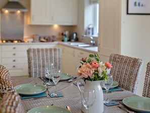 A dining area with a table set for two, a vase with flowers, and wicker chairs. - 4 Bed in Bideford (oc-85367) (Westward Ho!)