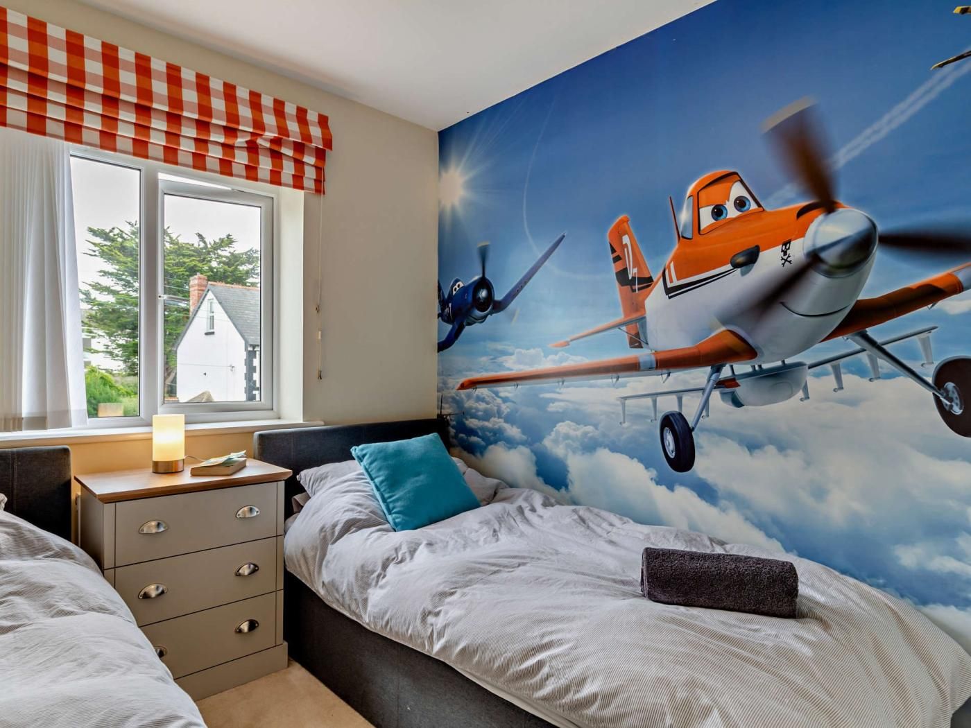 Una camera da letto con un grande murale di aerei animati, una finestra vista casa e un comodino con una lampada.