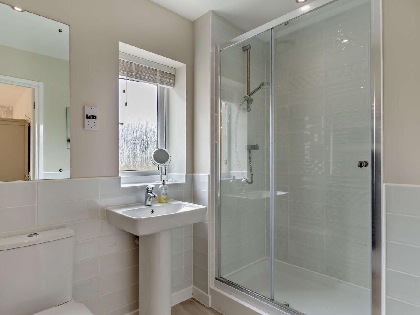 A bathroom with a glass-enclosed shower, a sink, and a mirror.