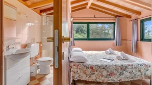Ein Schlafzimmer mit Bett, Fenster und einem Badezimmer mit Waschbecken und Toilette.