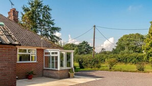 Ein eingeschossiges Backsteinhhaus mit einer überdachten Veranda, einer Schotterauffahrt und blauem Himmel.