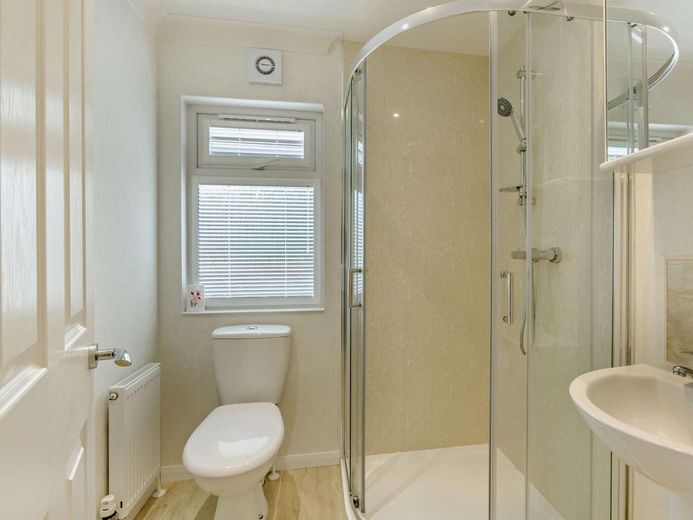 Une salle de bain moderne avec une douche à parois de verre, des toilettes, un lavabo et une fenêtre avec des stores.