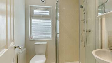 Une salle de bain moderne avec une douche à parois de verre, des toilettes, un lavabo et une fenêtre avec des stores.