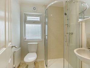 A modern bathroom with a glass shower enclosure, a toilet, a sink, and a window with blinds.
