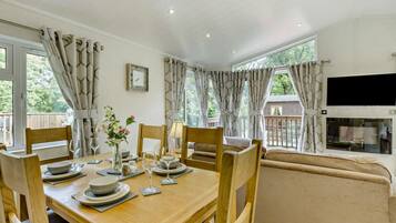 Un coin repas avec une table en bois dressée pour quatre personnes, des chaises, un vase avec des fleurs et un canapé en arrière-plan.