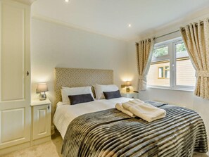 A bedroom with a bed, two bedside tables, a window with curtains, and a patterned headboard.