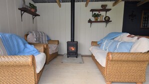 A cozy room with wicker furniture, a central wood-burning stove, and shelves with decorative items. - 1 Bed in Llandysul (oc-85415) (Rhydowen)