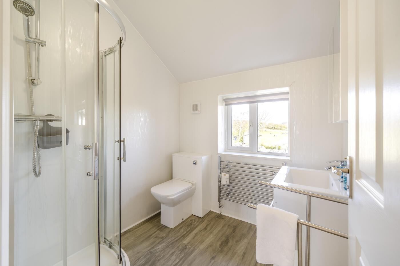 Une salle de bain équipée d’une douche, de toilettes et d’un lavabo, avec une fenêtre laissant entrer la lumière naturelle.