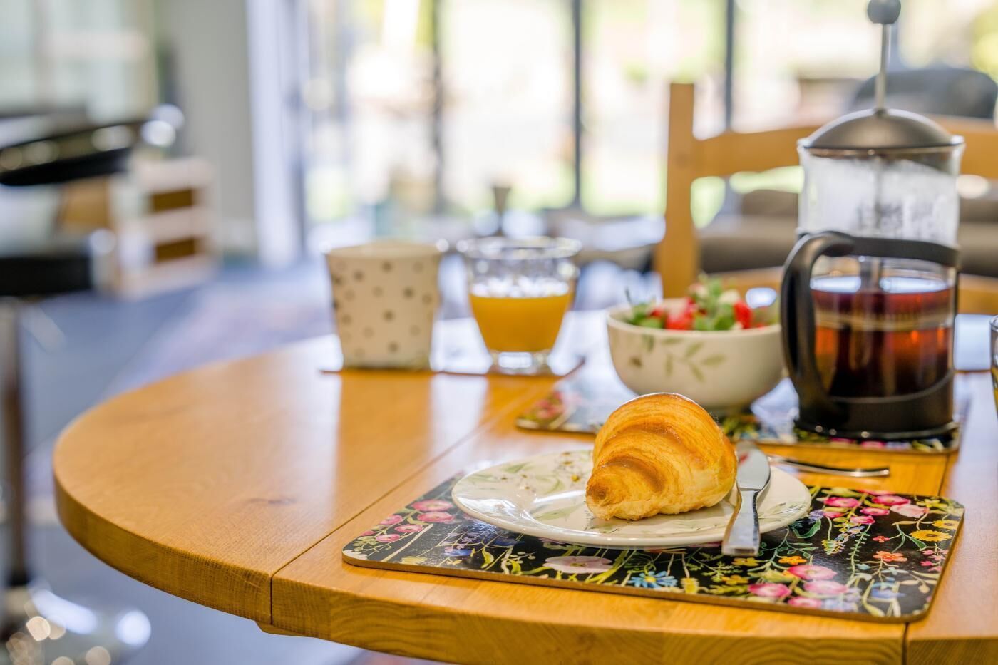 En frukostuppsättning med en croissant, kaffe, juice och en skål med sallad på ett träbord.