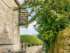A stone building with a sign for 'Theakston Black Bill Brewery' and a lush green hedge in the foreground. - 2 Bed in Ripon (oc-85510) (Masham)