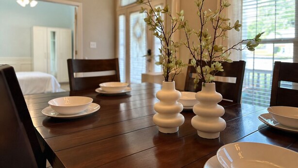 Une table à manger avec de l’assiette et des bols blancs, ainsi que deux vases blancs ornés de branches.
