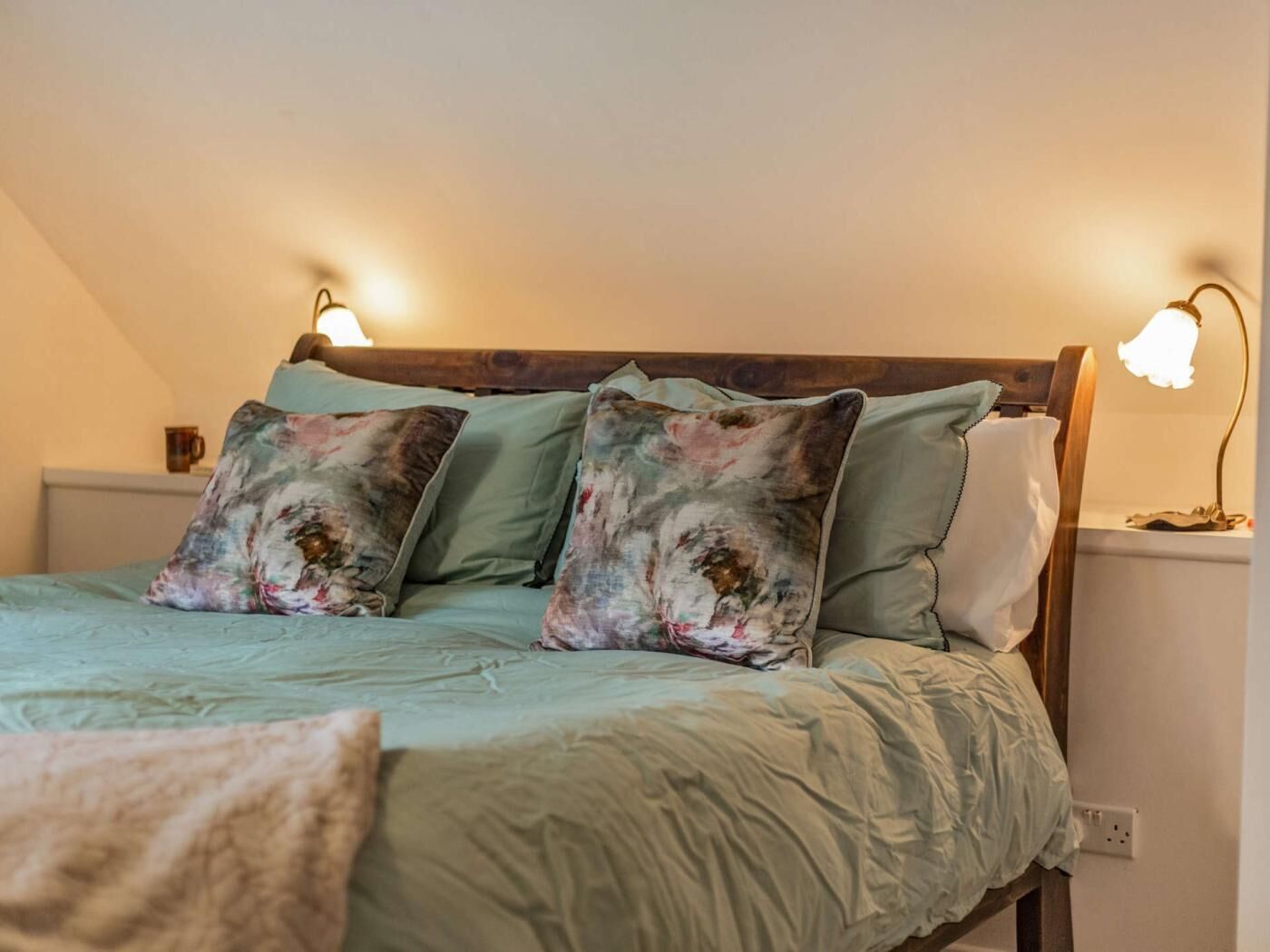 A bed with a wooden headboard, two wall-mounted lamps, and a green bedspread.