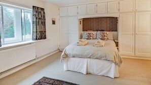 Ein Schlafzimmer mit einem Bett, einem Fenster mit Vorhängen, einem Heizkörper und eingebauten Schränken.