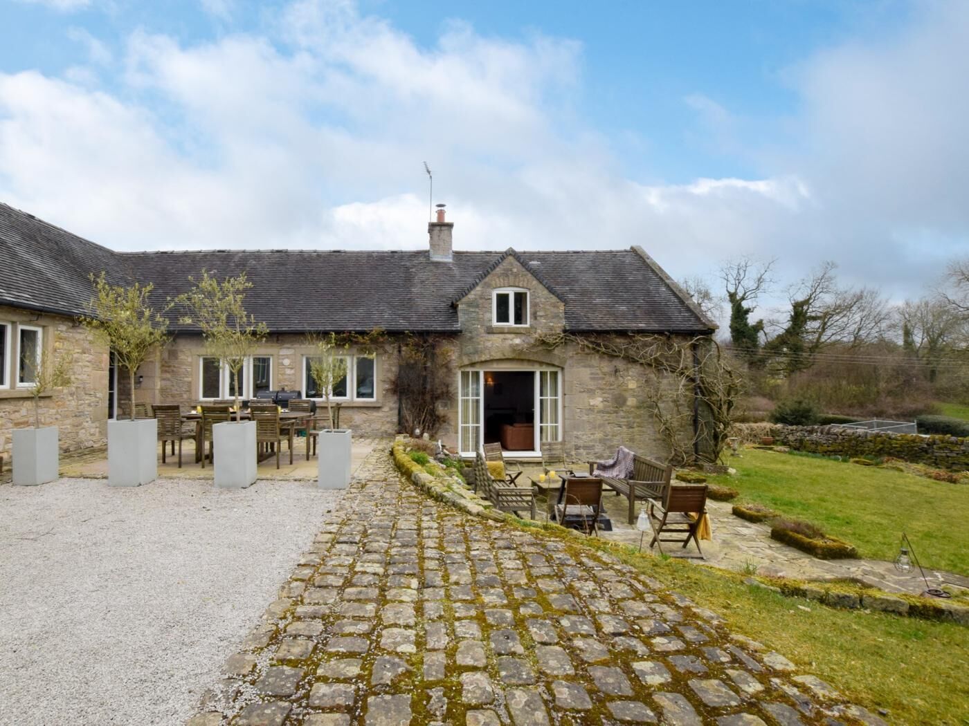 A stone house with a gravel driveway, outdoor seating, and a garden.